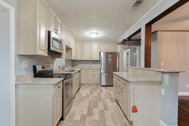 kitchen with light stone counters, visible vents, a sink, stainless steel appliances, and a textured ceiling