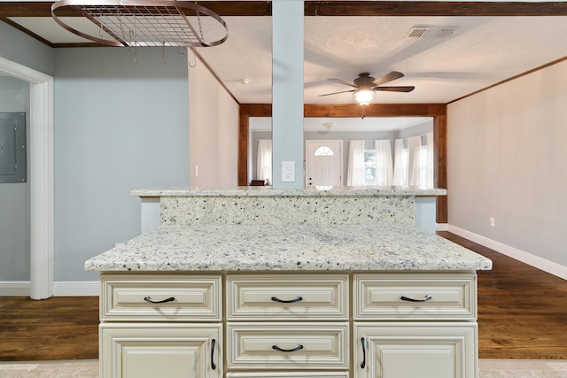 kitchen featuring light stone counters, cream cabinetry, dark wood-type flooring, and electric panel