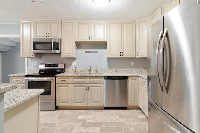 kitchen featuring cream cabinetry, appliances with stainless steel finishes, light stone countertops, and a sink