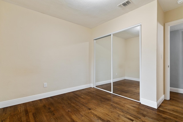 unfurnished bedroom with visible vents, baseboards, a closet, and dark wood finished floors