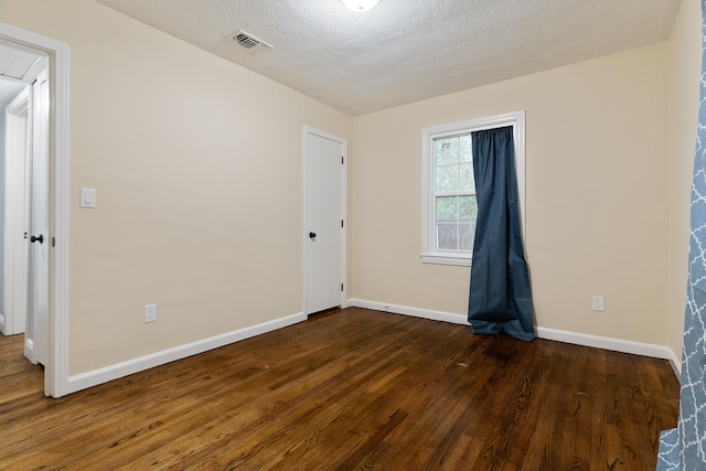 unfurnished room featuring visible vents, baseboards, a textured ceiling, and dark wood-style flooring