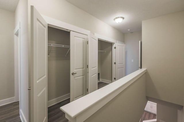 corridor featuring an upstairs landing, baseboards, and dark wood-style floors