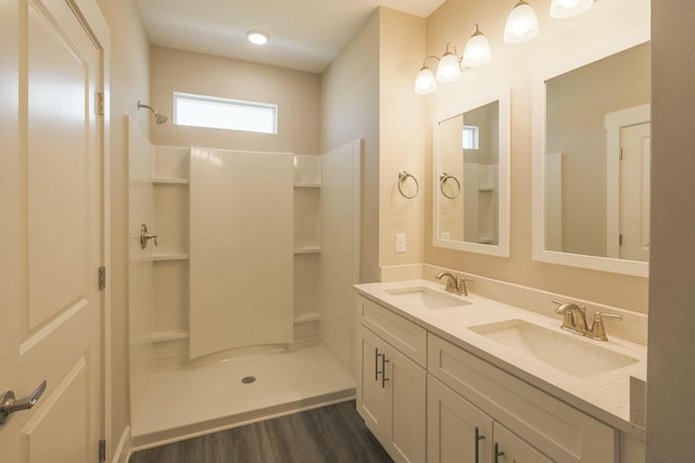 bathroom featuring wood finished floors, a walk in shower, double vanity, and a sink