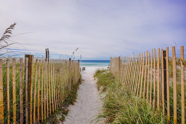 property view of water featuring a view of the beach and fence