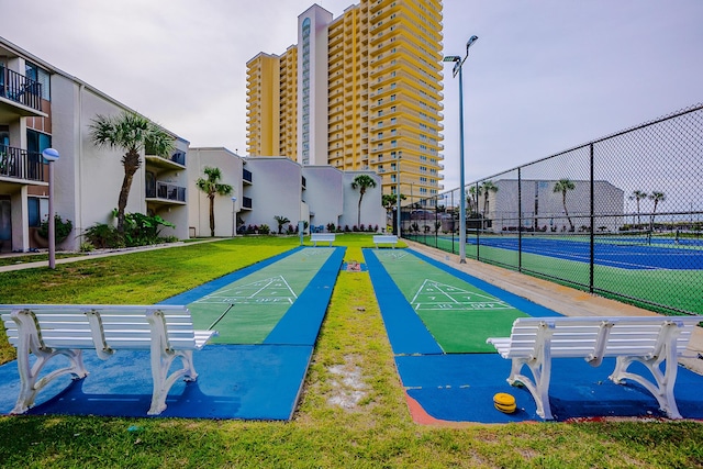 view of property's community with shuffleboard, a tennis court, a lawn, and fence