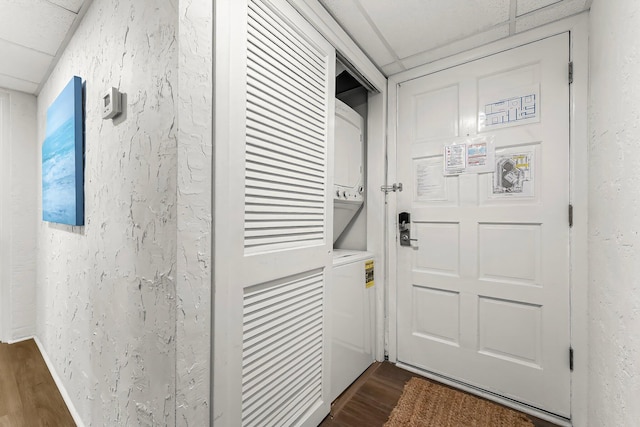 doorway with a drop ceiling, stacked washer and clothes dryer, dark wood-type flooring, and a textured wall