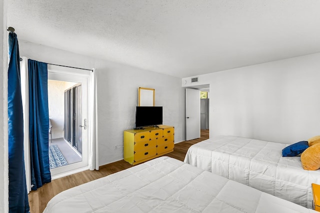 bedroom with access to exterior, wood finished floors, visible vents, and a textured ceiling