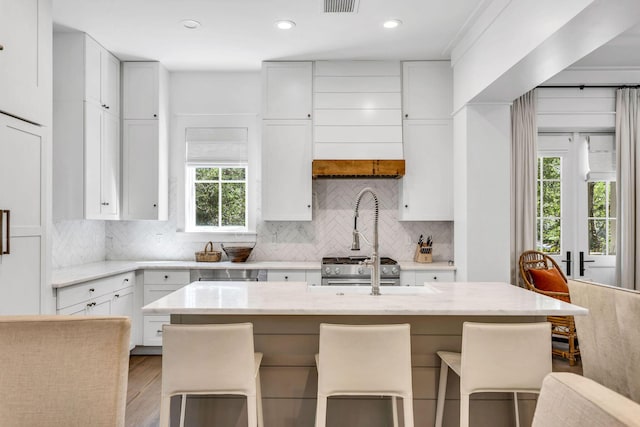 kitchen with light stone counters, wood finished floors, white cabinetry, a kitchen breakfast bar, and tasteful backsplash