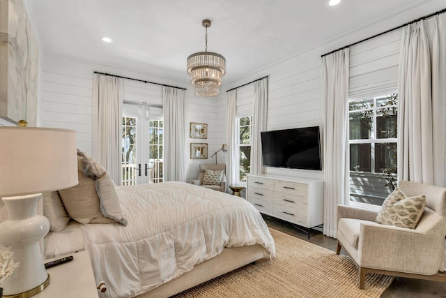 bedroom with wooden walls, wood finished floors, an inviting chandelier, recessed lighting, and french doors