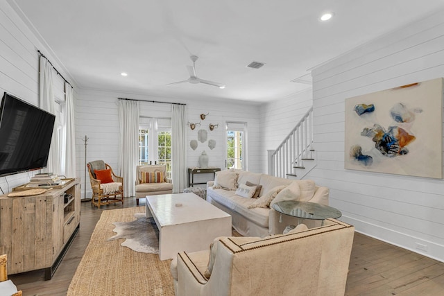 living area with visible vents, baseboards, stairway, wood finished floors, and a ceiling fan