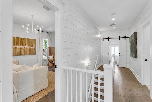 hallway featuring a barn door, wood finished floors, visible vents, and ornamental molding