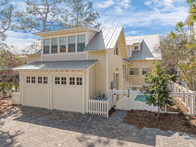 view of front of house with a standing seam roof, a garage, a fenced front yard, decorative driveway, and metal roof