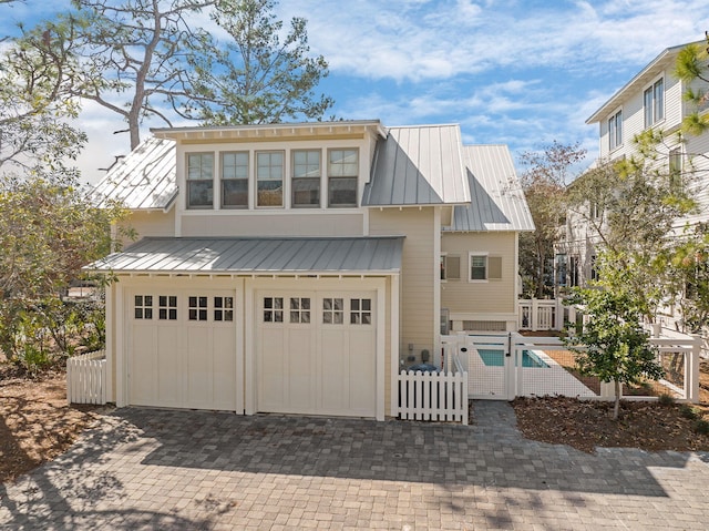 view of front of property with fence, metal roof, decorative driveway, a garage, and a standing seam roof