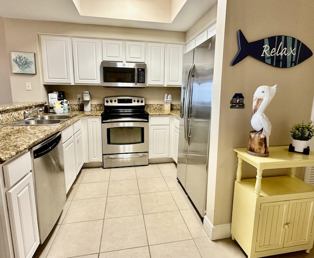 kitchen with light tile patterned floors, light stone counters, appliances with stainless steel finishes, white cabinets, and a sink