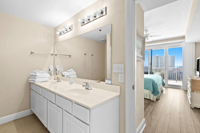 full bathroom with baseboards, ceiling fan, double vanity, ensuite bathroom, and a sink