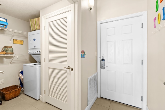 laundry room with visible vents, light tile patterned flooring, stacked washer / drying machine, baseboards, and laundry area