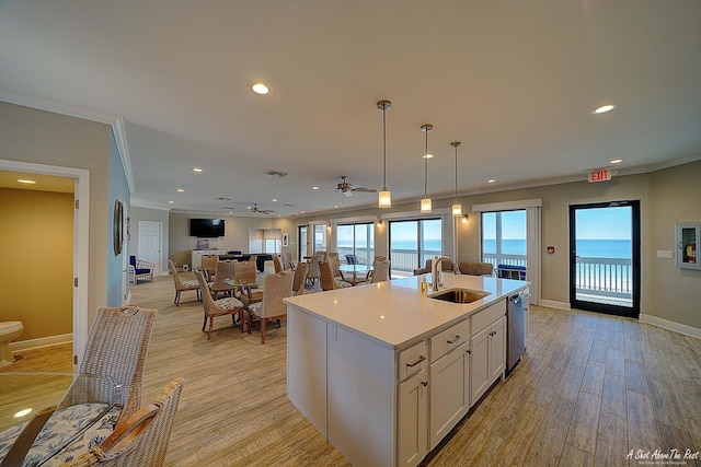 kitchen featuring light wood finished floors, ornamental molding, a sink, light countertops, and open floor plan