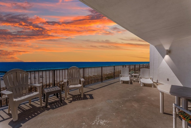 patio terrace at dusk with a view of the beach, a balcony, and a water view