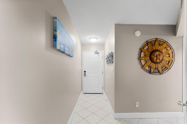 hallway featuring light tile patterned floors, baseboards, and a textured ceiling