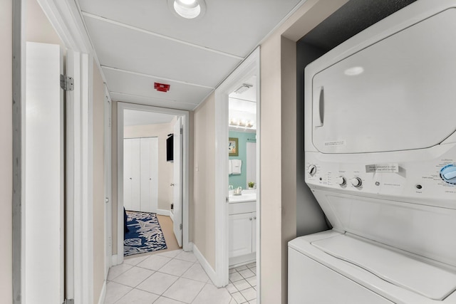 laundry area featuring light tile patterned floors, stacked washer / dryer, laundry area, and baseboards