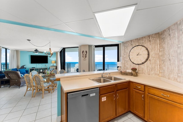 kitchen with a sink, stainless steel dishwasher, open floor plan, light tile patterned flooring, and brown cabinetry