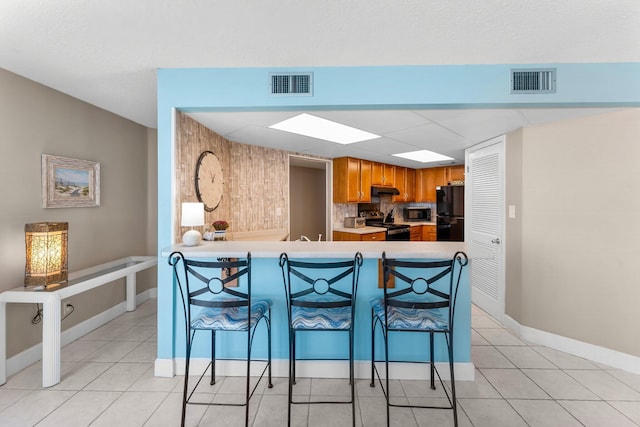 kitchen featuring under cabinet range hood, visible vents, brown cabinets, and black appliances