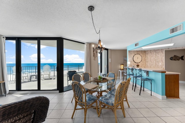 dining room with expansive windows, light tile patterned floors, visible vents, a water view, and a textured ceiling