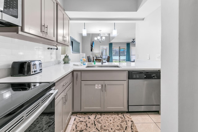 kitchen with a sink, gray cabinetry, appliances with stainless steel finishes, a notable chandelier, and tasteful backsplash