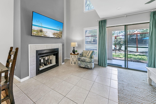 interior space with light tile patterned flooring, a tile fireplace, a high ceiling, and baseboards