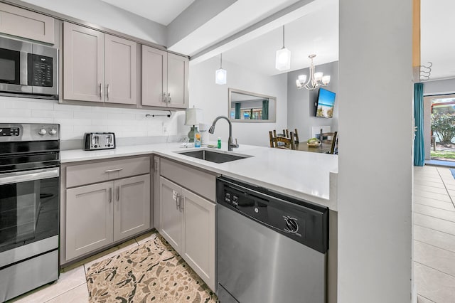 kitchen featuring gray cabinets, a sink, decorative backsplash, light countertops, and appliances with stainless steel finishes