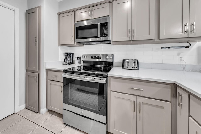 kitchen with light tile patterned flooring, decorative backsplash, gray cabinets, and stainless steel appliances