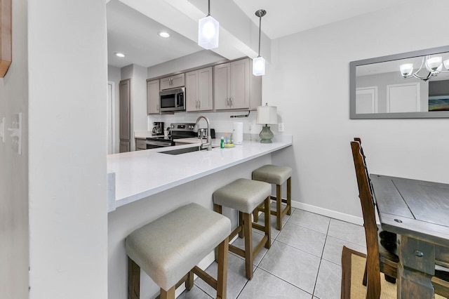 kitchen with stainless steel appliances, a kitchen bar, gray cabinetry, and light countertops