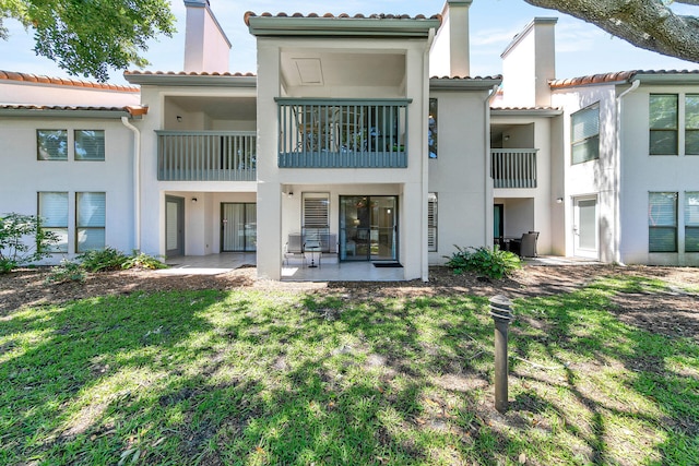 back of house featuring stucco siding, a chimney, a tile roof, a patio area, and a lawn