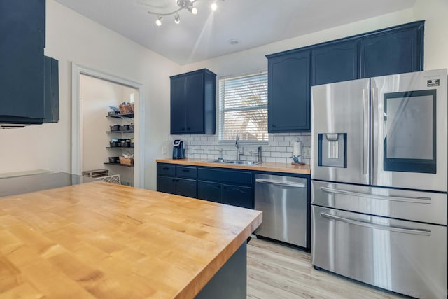 kitchen with blue cabinetry, a sink, stainless steel appliances, butcher block counters, and decorative backsplash