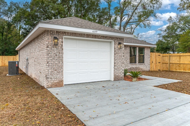 garage with central AC unit, concrete driveway, and fence