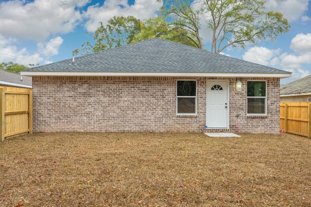 back of house featuring fence, brick siding, roof with shingles, and a lawn