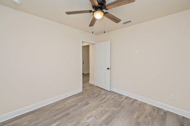 empty room featuring visible vents, light wood-style flooring, a ceiling fan, and baseboards