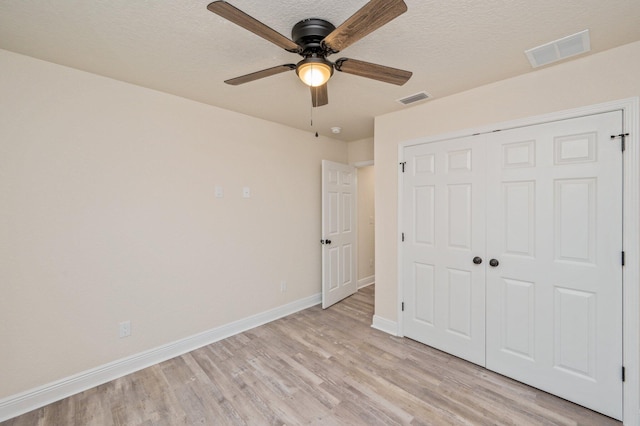 unfurnished bedroom with light wood finished floors, visible vents, a textured ceiling, and baseboards