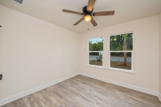 empty room with a ceiling fan, wood finished floors, visible vents, and baseboards