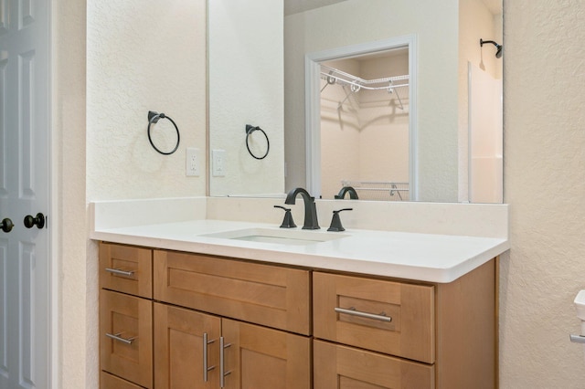 bathroom featuring vanity, a walk in closet, and a textured wall