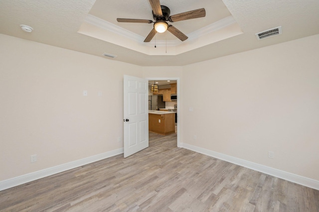 empty room with a tray ceiling, light wood-style flooring, and baseboards