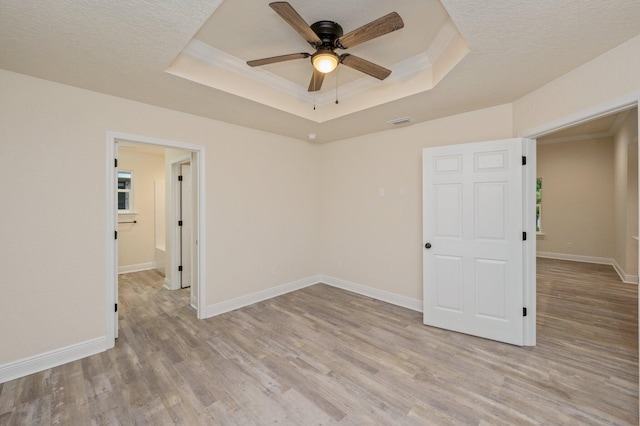 empty room featuring visible vents, crown molding, light wood-style floors, and a tray ceiling