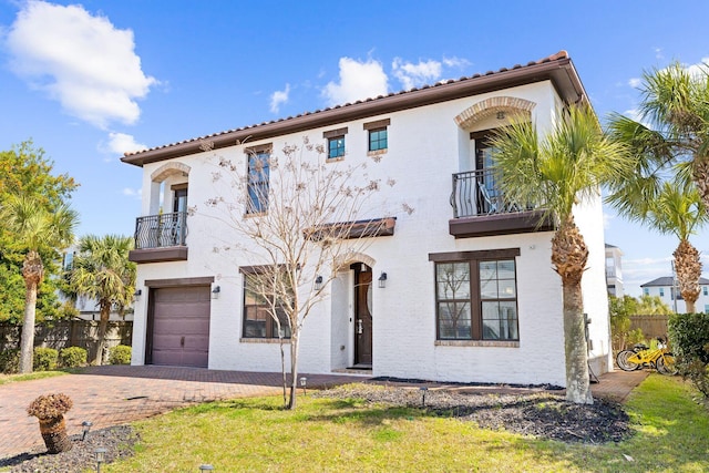 mediterranean / spanish home featuring fence, stucco siding, decorative driveway, a balcony, and an attached garage