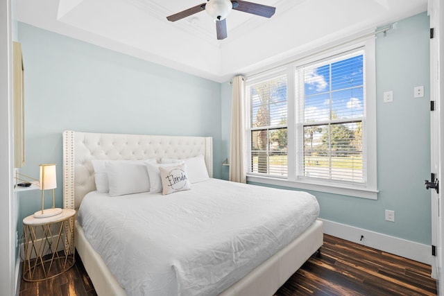 bedroom with baseboards, dark wood-style flooring, ornamental molding, ceiling fan, and a raised ceiling