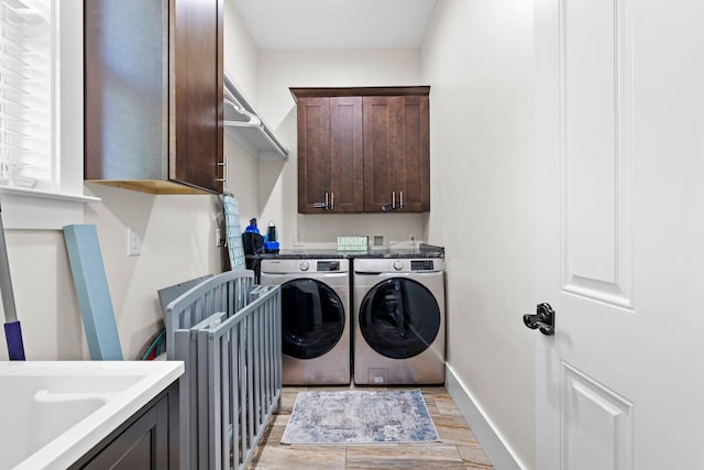 laundry room featuring washing machine and clothes dryer, cabinet space, baseboards, and light wood-style floors