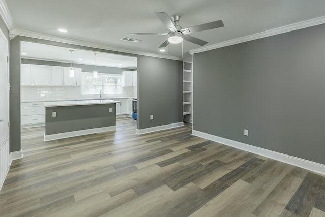 unfurnished living room featuring crown molding, ceiling fan, baseboards, wood finished floors, and a sink