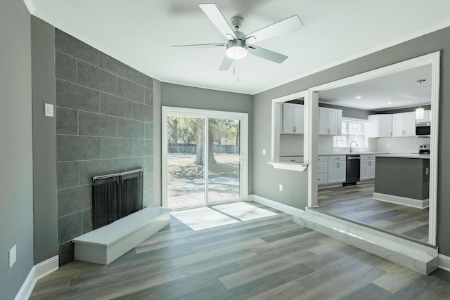 unfurnished living room featuring light wood-type flooring, a large fireplace, crown molding, baseboards, and ceiling fan