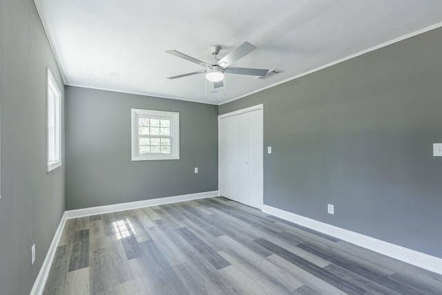 empty room with crown molding, wood finished floors, baseboards, and visible vents