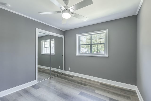 unfurnished bedroom featuring crown molding, baseboards, wood finished floors, a closet, and a ceiling fan