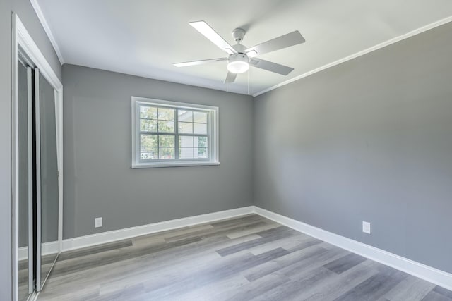 unfurnished bedroom with ornamental molding, wood finished floors, a closet, baseboards, and ceiling fan